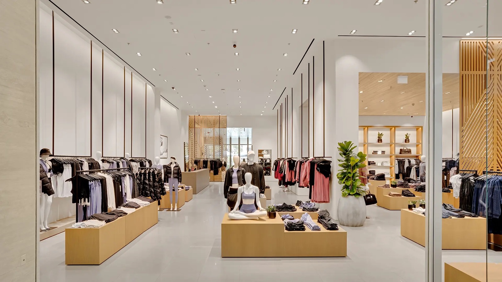 An Alo retail store interior: white walls, wooden plinths, racks of apparel and folded stacks