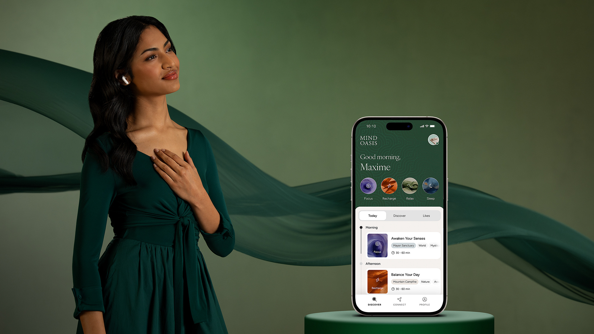 A woman in a green dress wearing earbuds, hand on her chest, beside a phone showing the Mind Oasis app greeting Good morning, Maxime