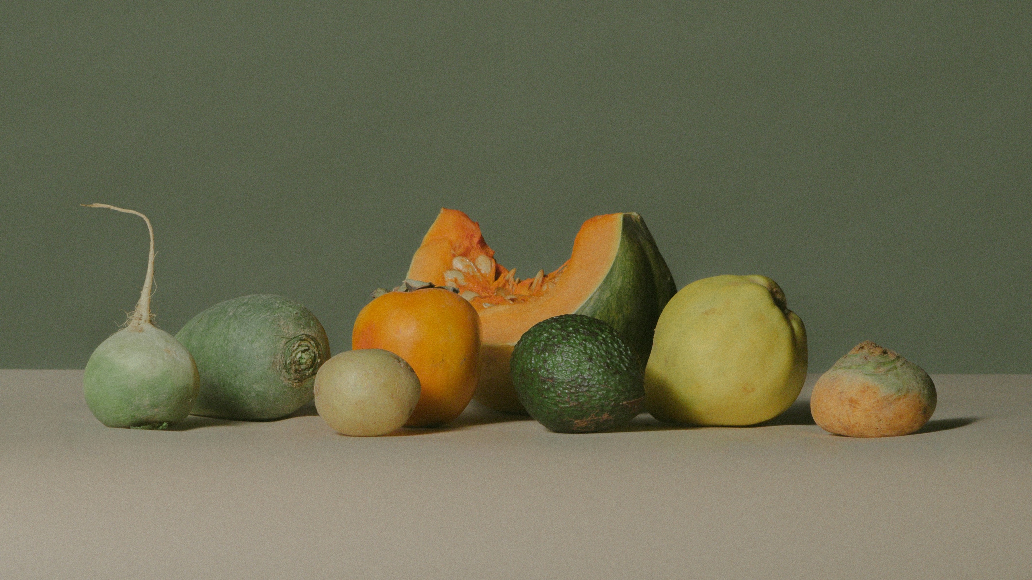 Still life of seasonal fruit and vegetables on a stone counter against a green wall